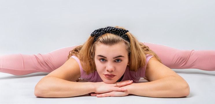 beautiful woman wearing pink sportswear stretching in a leg-split pose in the studio isolated on gray background