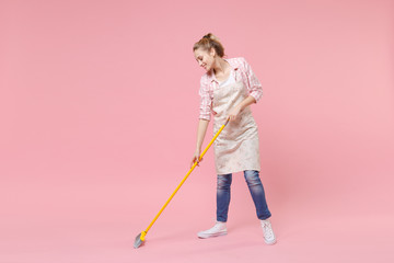 Smiling pretty young woman housewife in casual clothes, apron doing housework isolated on pastel...