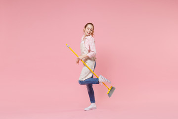 Cheerful pretty young woman housewife in casual clothes, apron doing housework isolated on pastel pink wall background studio portrait. Housekeeping concept. Mock up copy space. Hold in hands broom.