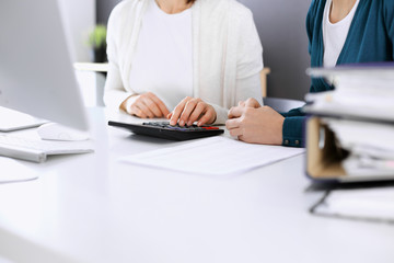 Fototapeta premium Accountant checking financial statement or counting by calculator income for tax form, hands closeup. Business woman sitting and working with colleague at the desk in office. Tax and Audit concept