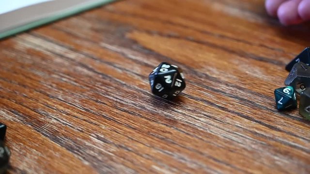 Slow motion hand rolling a d20 black dice that lands on 20