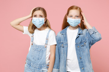 Displeased sick two little kid girls 12-13 years old in sterile face mask isolated on pink background studio. Epidemic pandemic coronavirus 2019-ncov sars covid-19 flu virus concept. Put hand on head.