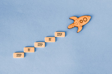 Concept of business development, startup, success. Rocket soaring up from the steps that say " step by step"