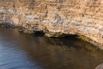rock, perennial limestone on a rocky stretch of shore. blue sea and rocky cliff backlit by the setting sun. mountain cliff and sea