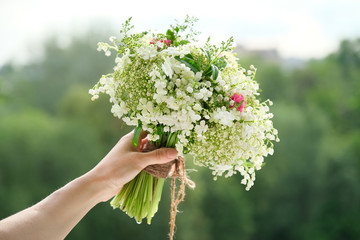 Fototapeta na wymiar Close-up bouquet of fresh flowers rose and lily of the valley in woman hand