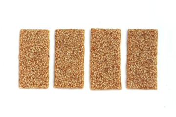 Close up of four sesame seed bars laid flat side by side on a white background