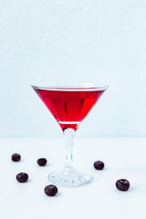 A bright red drink in a cocktail martini glass, blueberries, light blue background, natural light vertical photo