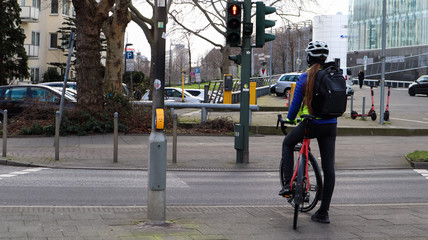 Germany, Dusseldorf - February 28, 2020: A young girl a cyclist in a helmet, stopped at a traffic light and waiting for a permission signal to cross the street. City view.