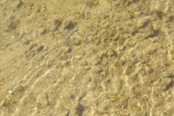 Fototapeta na wymiar Close up view of stream bottom with sand and stone. Water is transparant and clean. Day is sunshining.