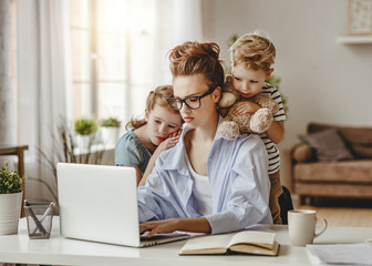 Calm little children embracing serious adult woman using laptop together at home.