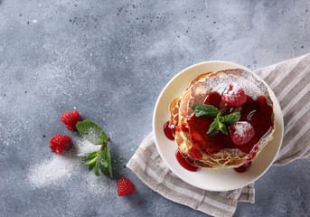 American cuisine. Breakfast. Pancakes with raspberries, sweet red topping, powdered sugar and mint in a white plate on a light grey background. Background image, copy space