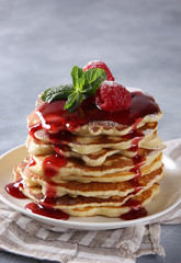 American cuisine. Breakfast. Pancakes with raspberries, sweet red topping, powdered sugar and mint in a white plate on a light grey background. Background image, copy space