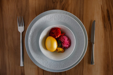 Easter table setting composition with traditional golden painted egg, beautiful tableware on natural dark wood textured table. Top view, copy space, close up, background.