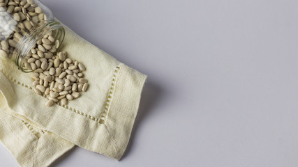 Beans in a glass jar on a cloth napkin. White background. Top view
