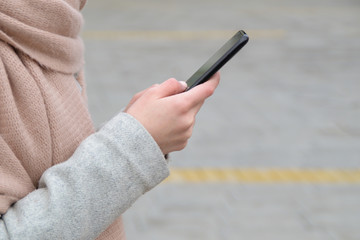 A woman's hand holds a smartphone outside on the street during cold weather. Copy space for text.