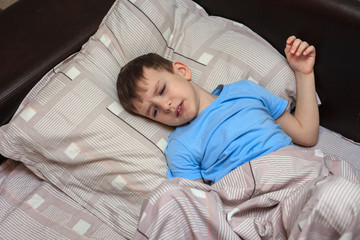 Child boy lies on the bed with a displeased face, is sick. Home quarantine. Virus. flu. Bed rest