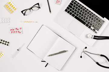Doctor work place with copyspace, stethoscope, laptop, notebook and medicine pills on table. Medicine and epidemic concept. Flat lay style