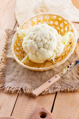 Cauliflower in a wicker basket on wooden background. Organic cauliflower on the burlap