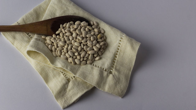 Beans On A Cloth Napkin And Wooden Spoon. White Background. Top View