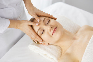 Obraz na płótnie Canvas Beautiful caucasian woman enjoying facial massage with closed eyes in spa salon. Relaxing treatment in medicine and Beauty concept