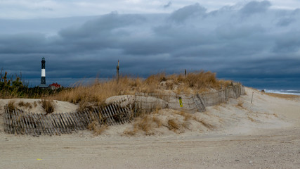 Beach with lighthouse, storm clouds and snow fencing