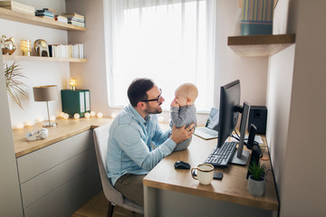 Young father working from home and babysitting his baby boy.