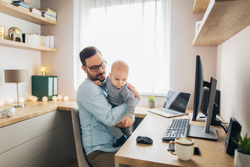 Young father working from home and holding his baby boy.