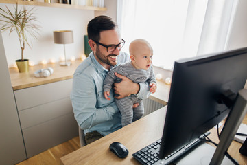 Young father working from home and holding his baby boy.