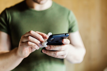 Disinfection the phone with an antiseptic using an antibacterial cloth. Close-up of hands holding a napkin with antiseptic, wiping the smartphone, covid-19 and coronavirus. Concept of personal hygiene