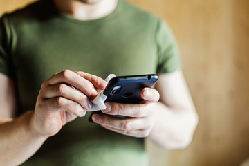 Disinfection the phone with an antiseptic using an antibacterial cloth. Close-up of hands holding a napkin with antiseptic, wiping the smartphone, covid-19 and coronavirus. Concept of personal hygiene