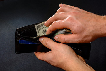 man removing dollars from his wallet, hands and wallet on black background.