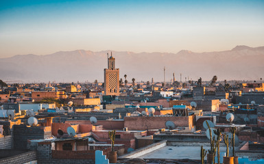 Panoramic sunset view of Marrakesh Mdina and the snow capped Atlas mountains in Morocco. View of rooftops of Marrakech close to the city centre. Koutoubia Mosque minaret during Sunrise on blue sky.