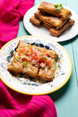 Mexican chimichanga with melted cheese and pico de gallo sauce on turquoise background