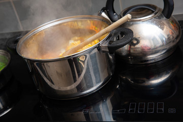 In the kitchen, colorful vegetables are cooked in a large nickel-plated pot.