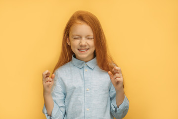 portrait of caucasian girl believing in the best, she crossed fingers and stand with closed eyes,...