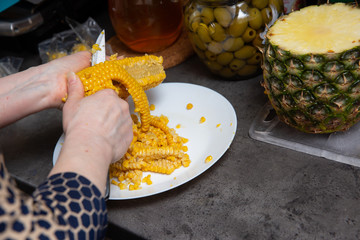 In the kitchen, scraping of boiled corn continues as an addition to a vegetable salad.
