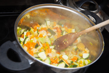 In the kitchen, colorful vegetables are cooked in a large nickel-plated pot.