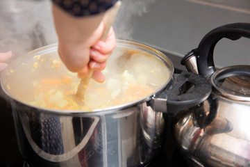 In the kitchen, colorful vegetables are cooked in a large nickel-plated pot.