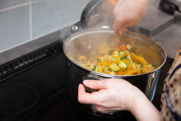 In the kitchen, colorful vegetables are cooked in a large nickel-plated pot.