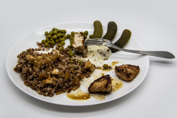 Started to eat delicious buckwheat porridge with chicken, green peas, cucumbers and sauce on a white plate. Almost empty plate with food. Healthy diet food with chicken meat.