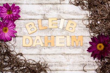 Bleib daheim - Holzbuchstaben vor Frühlungs-Hintergrund