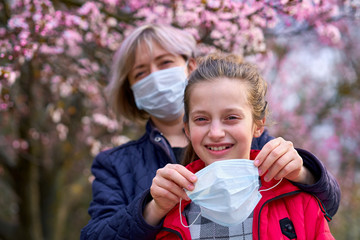 mother and daughter with a face mask are in the city outdoor, blooming trees, spring season,...