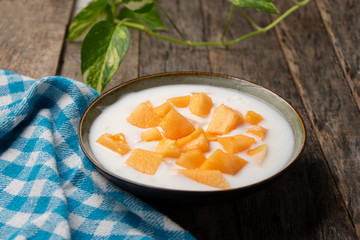 Cantaloupe melon with yogurt in bowl on wooden background