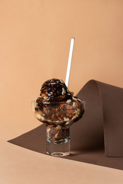helado de chocolate sobre fondo caf&eacute; y beige en monocromia con cuchara y salsa de chocolate con trozos de almendra