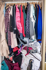 Sloppy things in the closet. Open wardrobe with clothes on hangers and clutter in open drawers