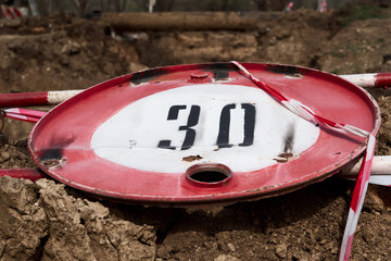 the road sign for the speed limit of thirty kilometers or miles per hour and the road fence for performing repair work lies on the ground