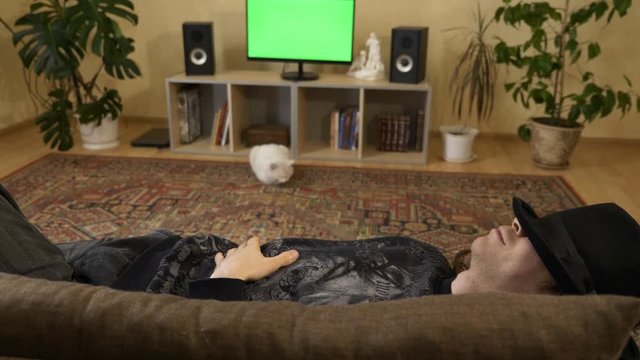 4K 60p Young Adult Male Lays On Couch Sofa Relaxing Enjoying In Front of Green Screen TV Listening To Music Loudly