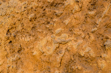 Fragment of the wall of an old house with a rough-faced cement plaster surface with overlays and influxes, painted in orange, peach and beige colors. Uneven staining. Abstract hard concrete background