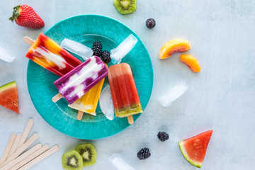 Top down view of a blue plate with delicious homemade fruit popsicles surrounded by fresh pieces of...