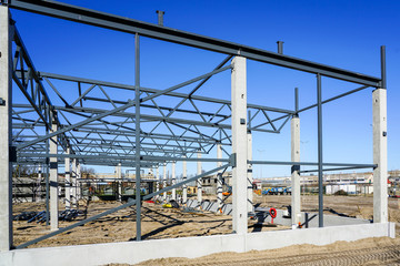 Fototapeta premium The steel frame of the new building with reinforced concrete supports is under construction